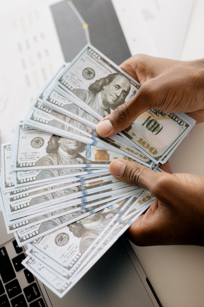Close-up view of hands counting U.S. hundred dollar bills over a laptop background.
