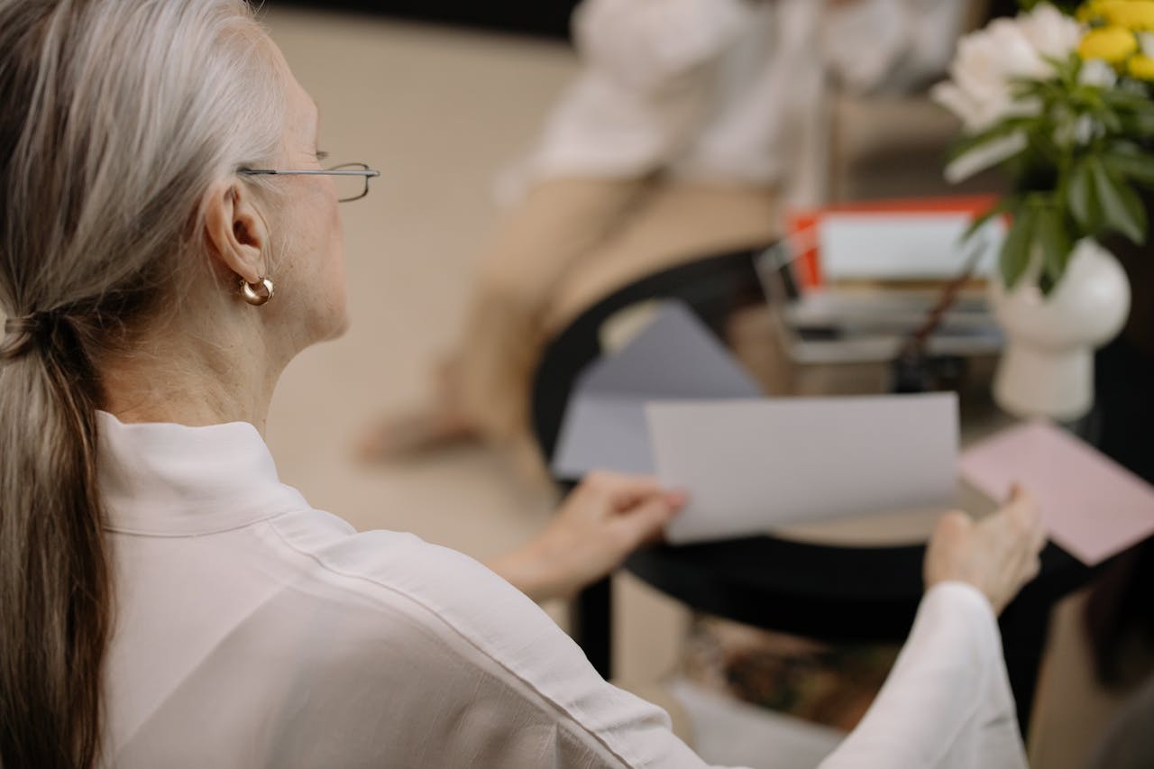An elderly woman examines papers from the comfort of her living room.