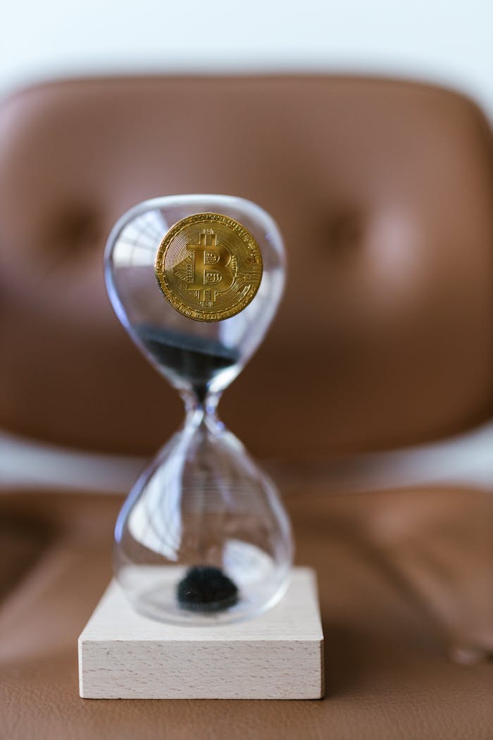 A Bitcoin coin inside an hourglass on a leather chair symbolizes time's impact on cryptocurrency.